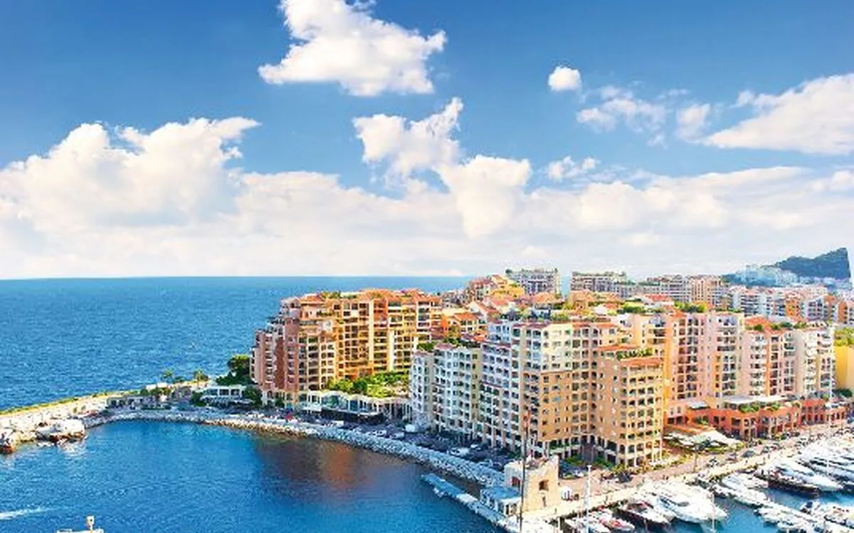Yachthafen von Monte Carlo mit Yachten, Gebäuden und Mittelmeer im Hintergrund.