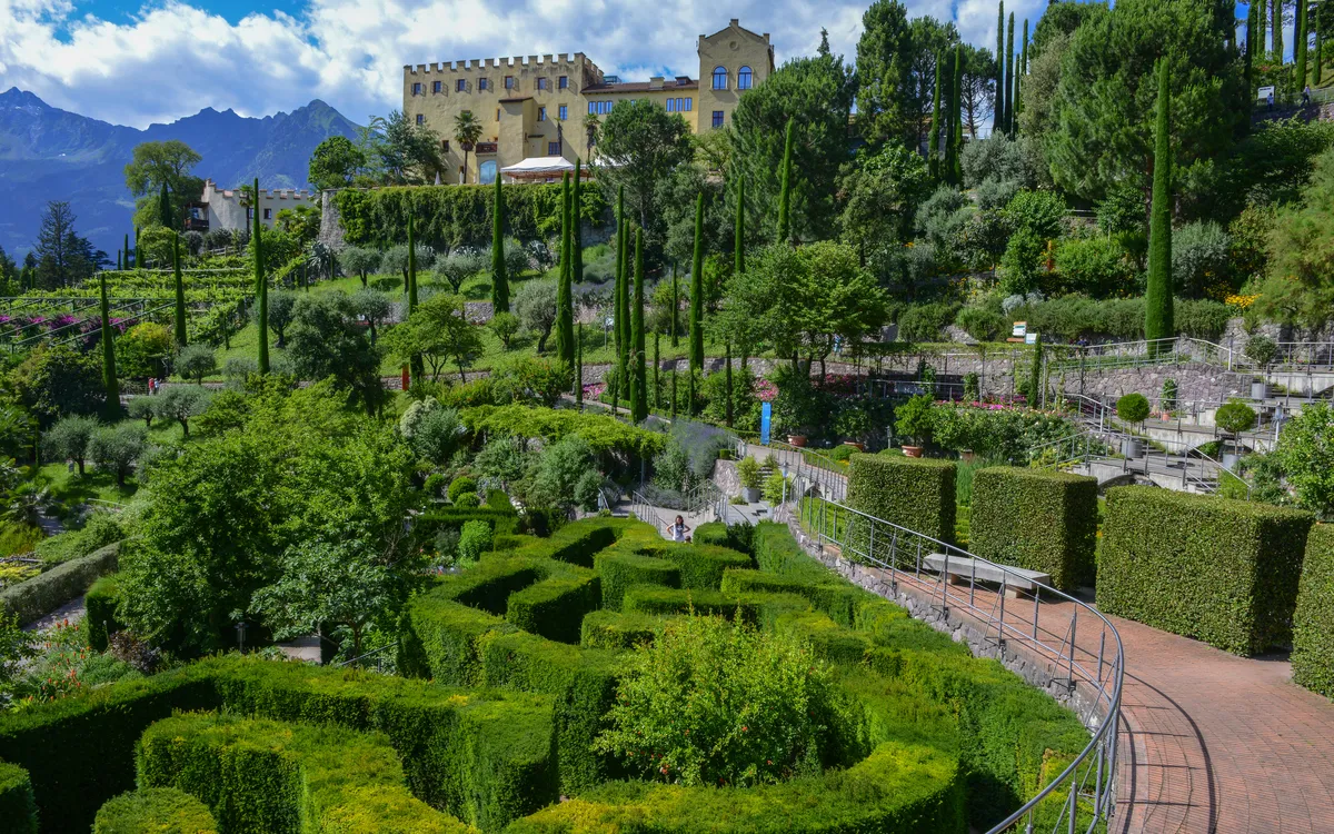 Historischer Garten mit Schloss und Labyrinth aus Hecken im Hintergrund.