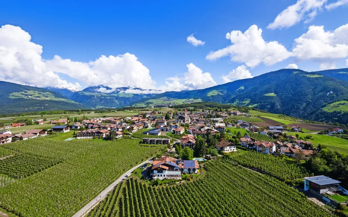 Luftaufnahme von Natz, Südtirol, mit Obstplantagen und Bergen im Hintergrund.