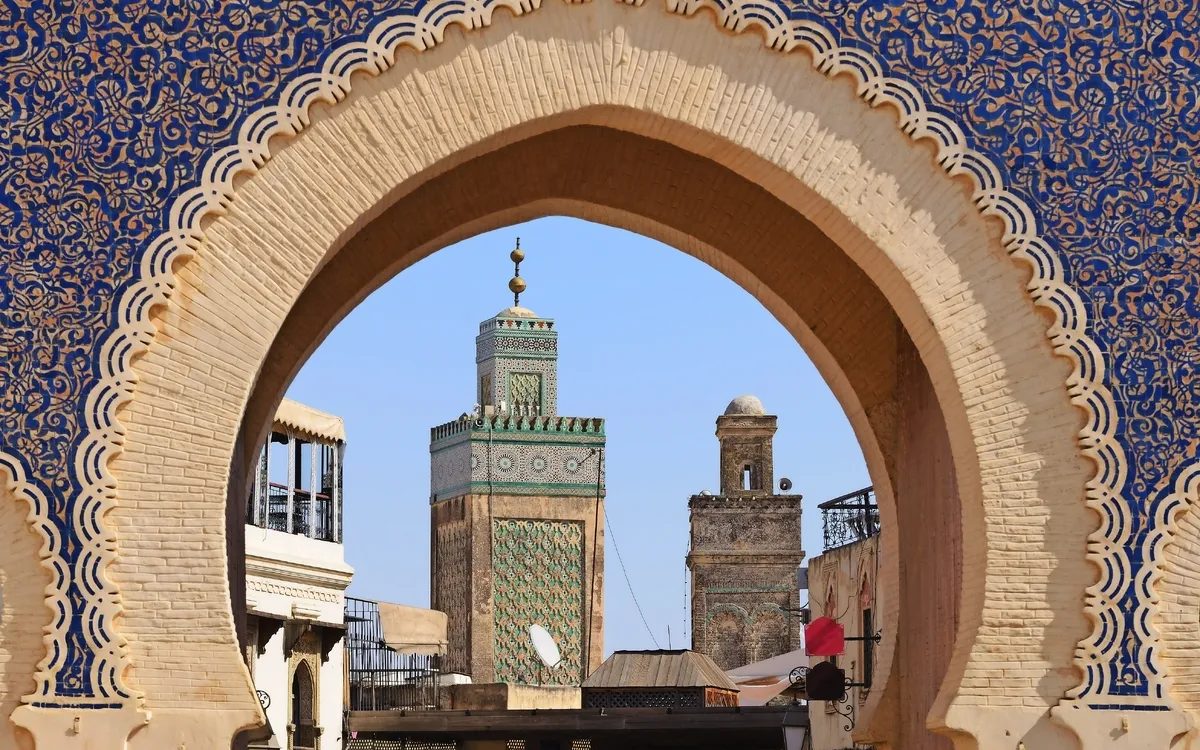 Blick durch ein verziertes Tor auf eine Moschee in der Altstadt von Fes, Marokko.