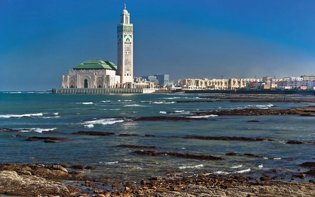 Hassan-II-Moschee an der Küste von Casablanca, mit blauem Himmel und Meer im Vordergrund.
