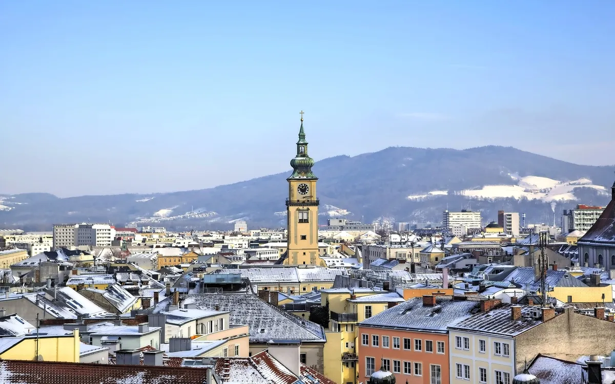 Stadtpanorama mit Kirchturm vor schneebedecktem Berg im Hintergrund.