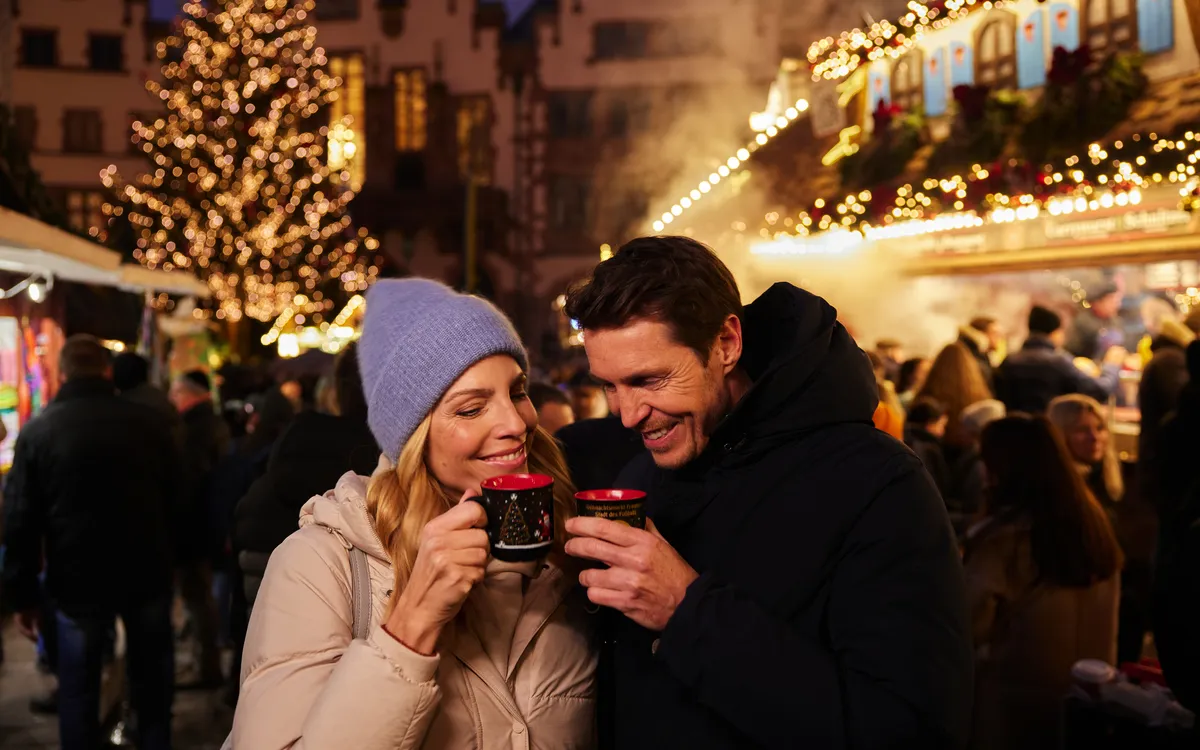 Paar trinkt heißen Glühwein auf einem festlich beleuchteten Weihnachtsmarkt.