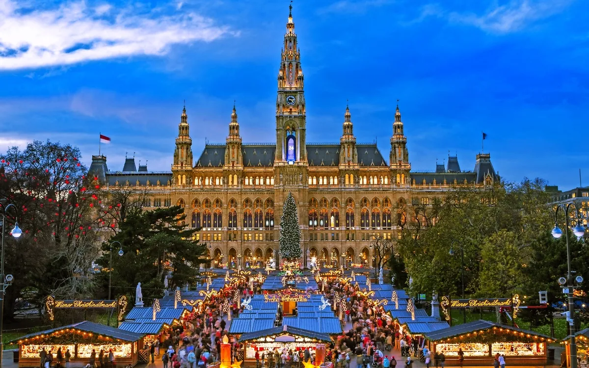 Weihnachtsmarkt vor einem beleuchteten, historischen Gebäude bei Dämmerung