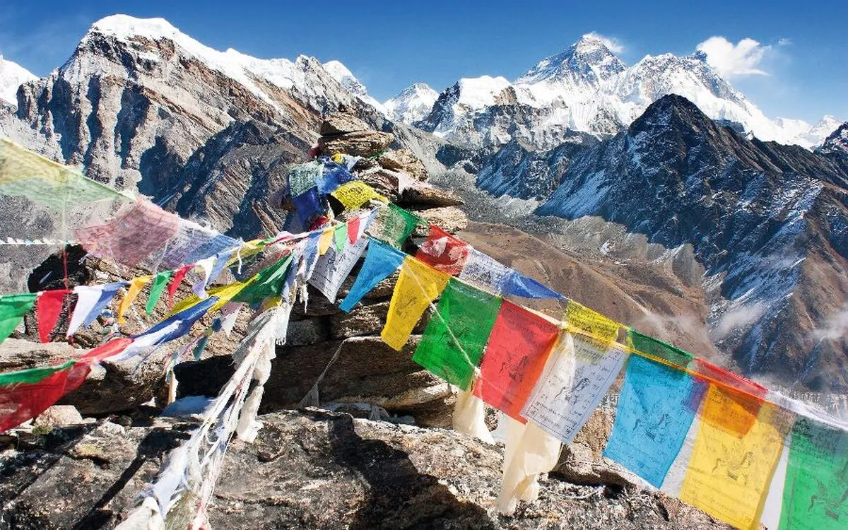 Bunte Gebetsflaggen wehen vor schneebedecktem Himalaya-Gipfel.