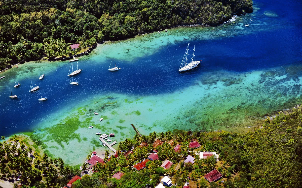 Luftaufnahme einer tropischen Küstenlandschaft mit Segelschiffen und dicht bewaldetem Hinterland