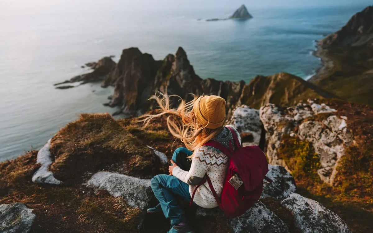 Person sitzt auf Klippe mit Blick auf Meer und Insel im Hintergrund.