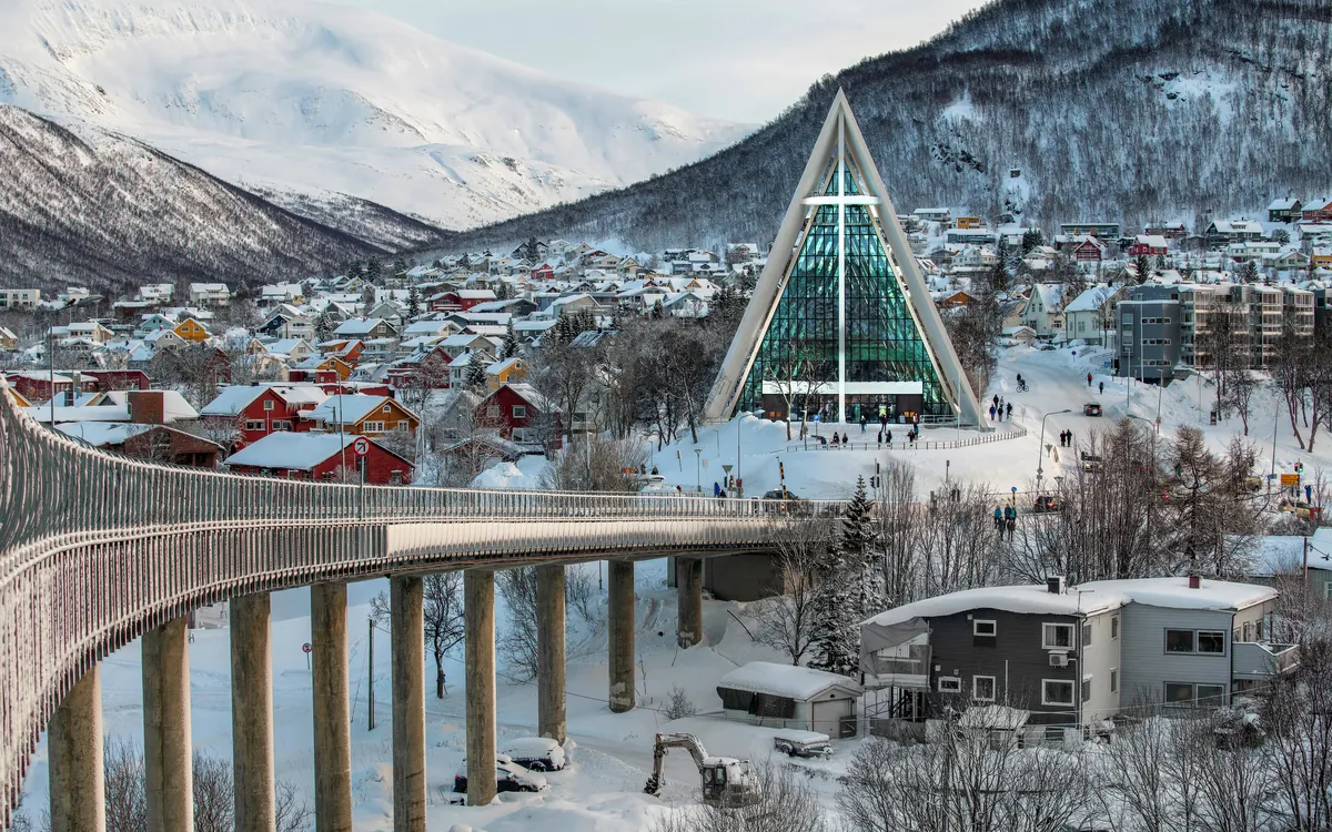 Verschneite Landschaft mit moderner Kirche und Brücke in winterlicher Stadt.