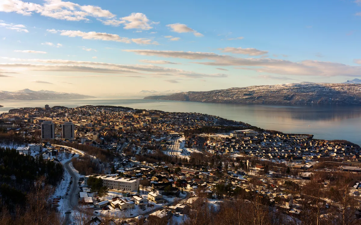 Luftaufnahme einer verschneiten Stadt am Fjord mit Bergen im Hintergrund.
