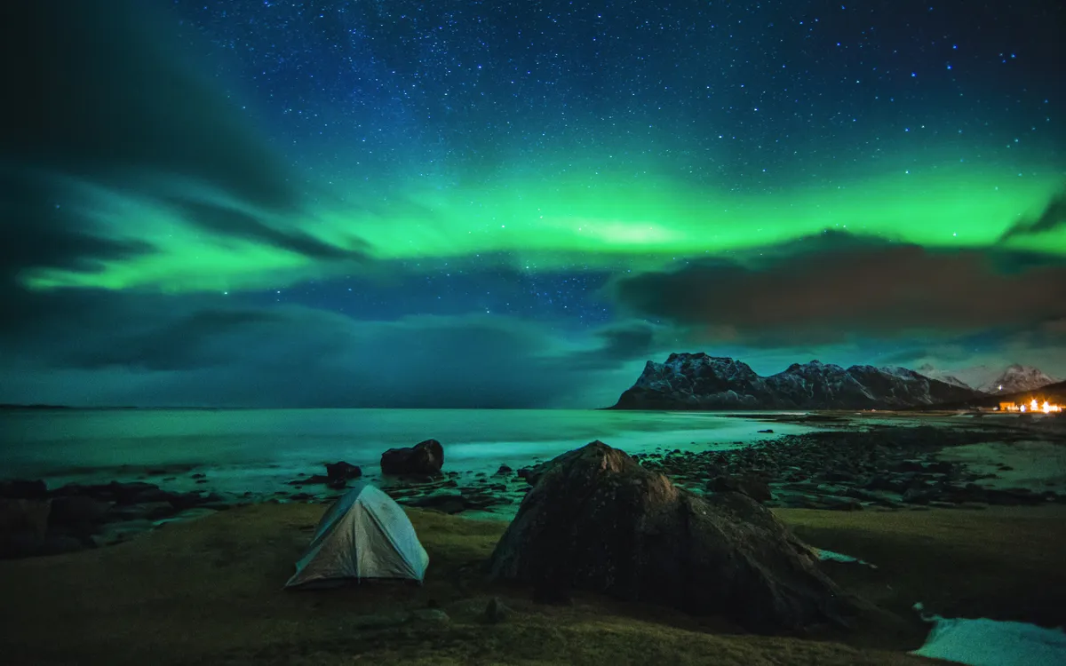 Zelt an einem Strand auf den Lofoten in Norwegen mit strahlenden Nordlichtern am Nachthimmel.