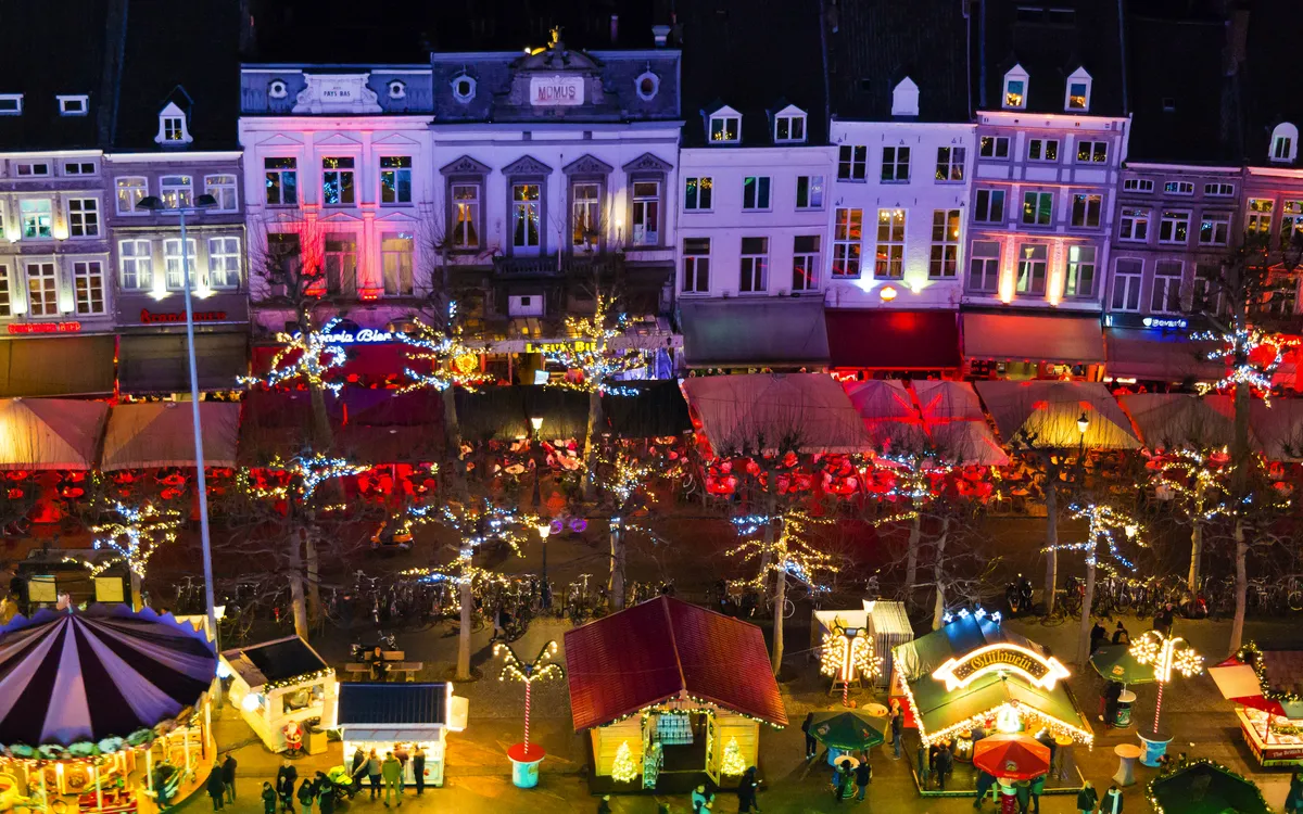 Blick auf einen beleuchteten Weihnachtsmarkt bei Nacht mit Ständen und Lichtern.