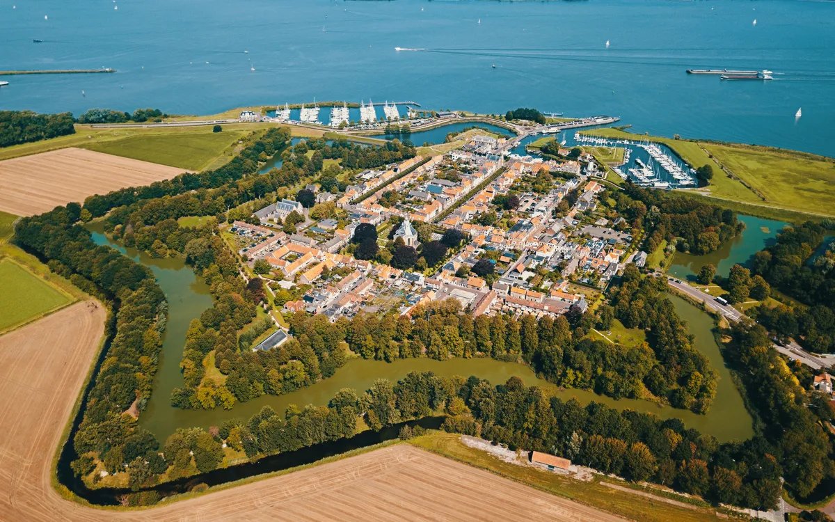 Luftaufnahme einer befestigten Stadt mit Wasser und Feldern im Hintergrund.