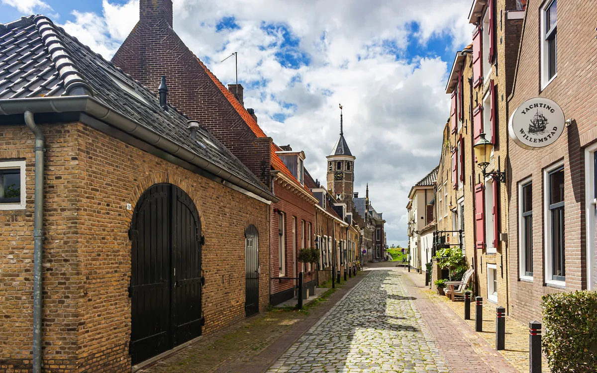 Pflastersteinstraße mit historischen Gebäuden und Kirchturm im Hintergrund.