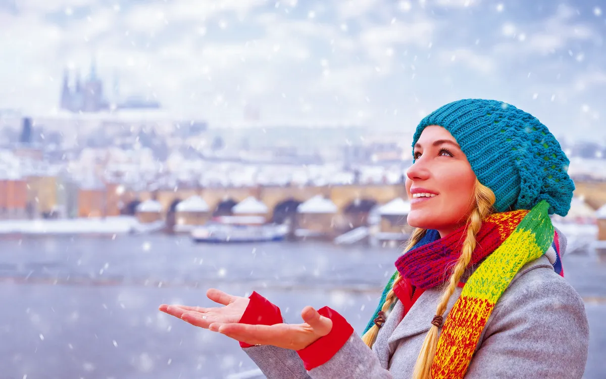Frau in Prag genießt Schneefall mit Blick auf Moldau und Brücke.