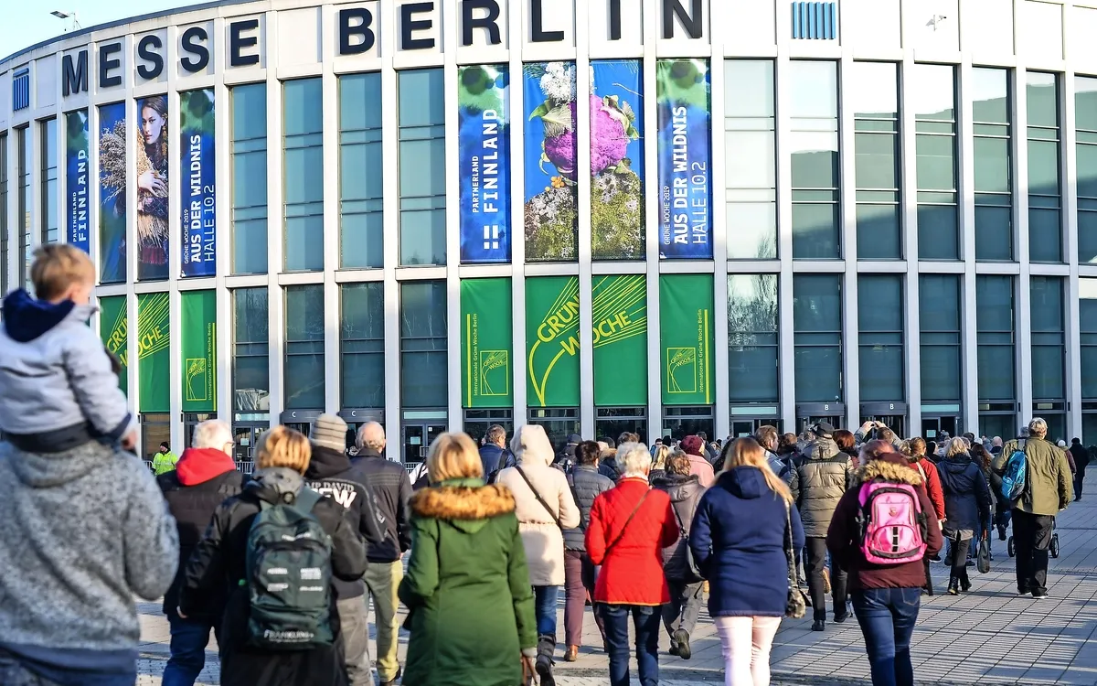 Menschen betreten die Messe Berlin mit Bannern der Grünen Woche am Gebäude.