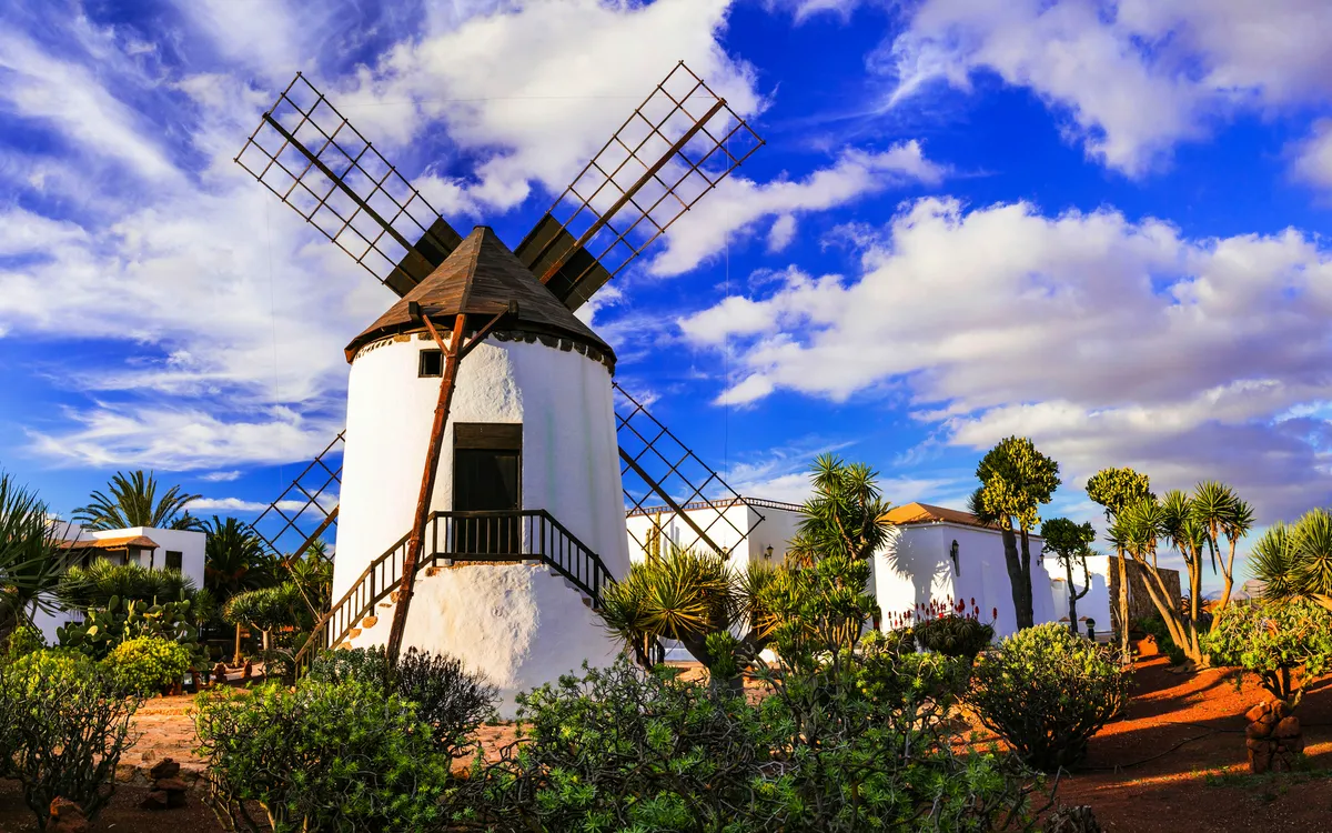 Traditionelle Windmühle in einer Landschaft mit blauem Himmel und Wolken.