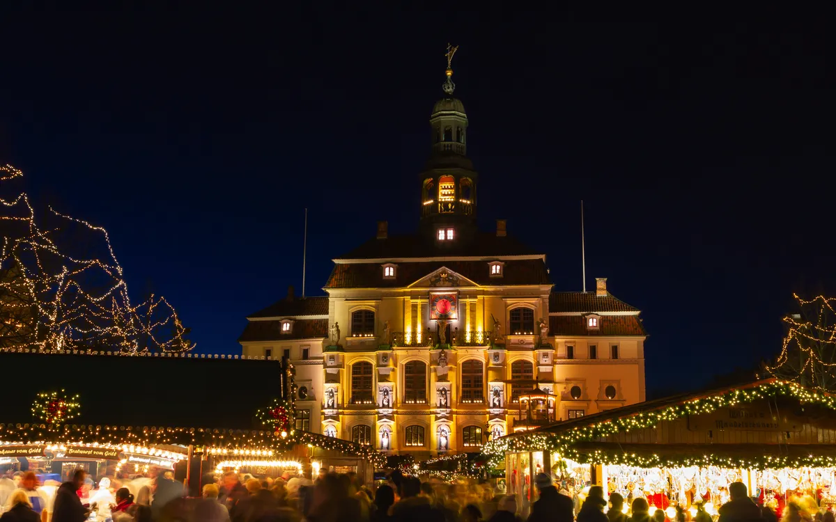 Weihnachtsmarkt vor dem beleuchteten historischen Rathaus in Lüneburg während des Winters.