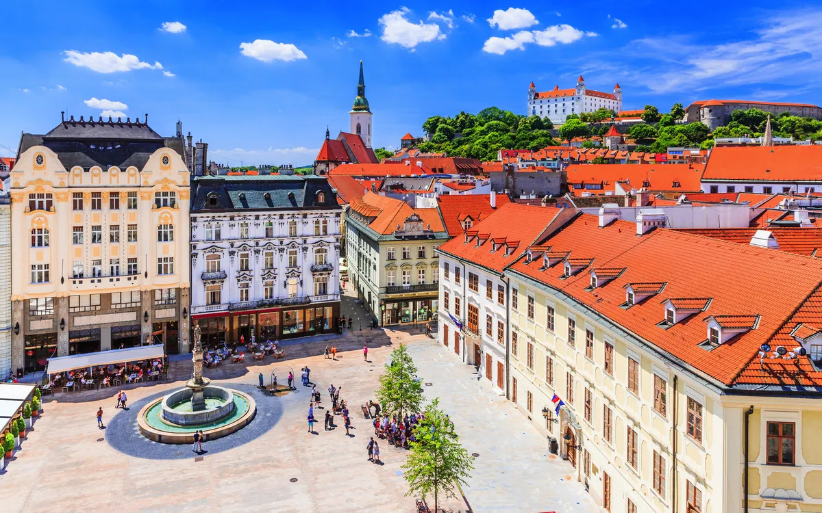 Städtischer Platz mit historischen Gebäuden und einem Schloss im Hintergrund.