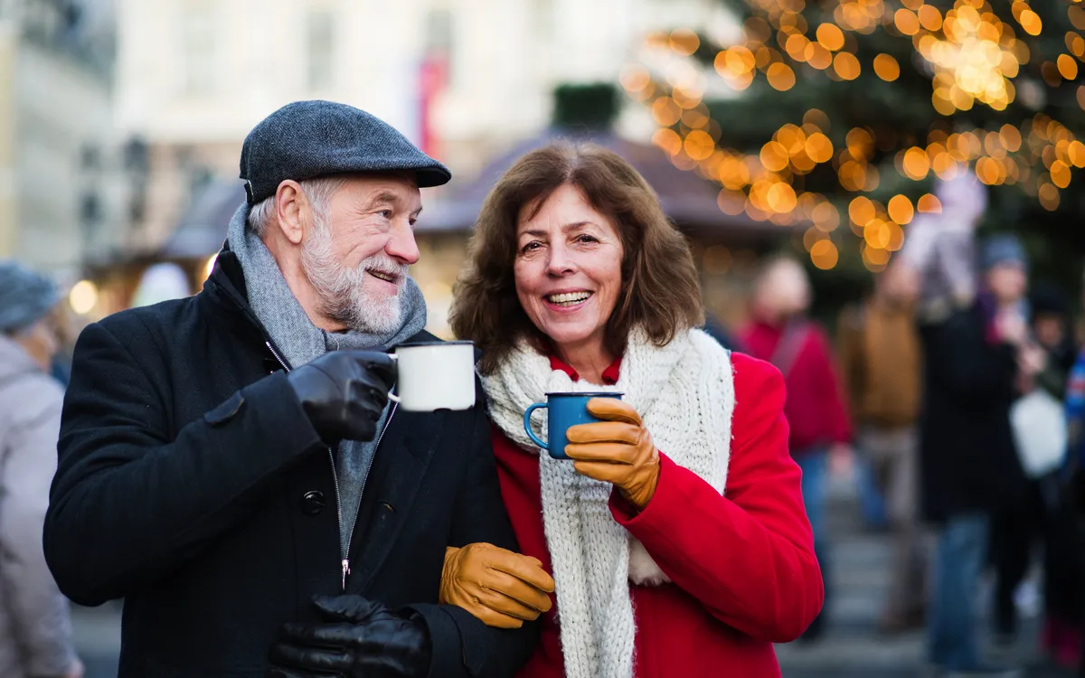 Älteres Paar trinkt Heißgetränke auf einem Weihnachtsmarkt.