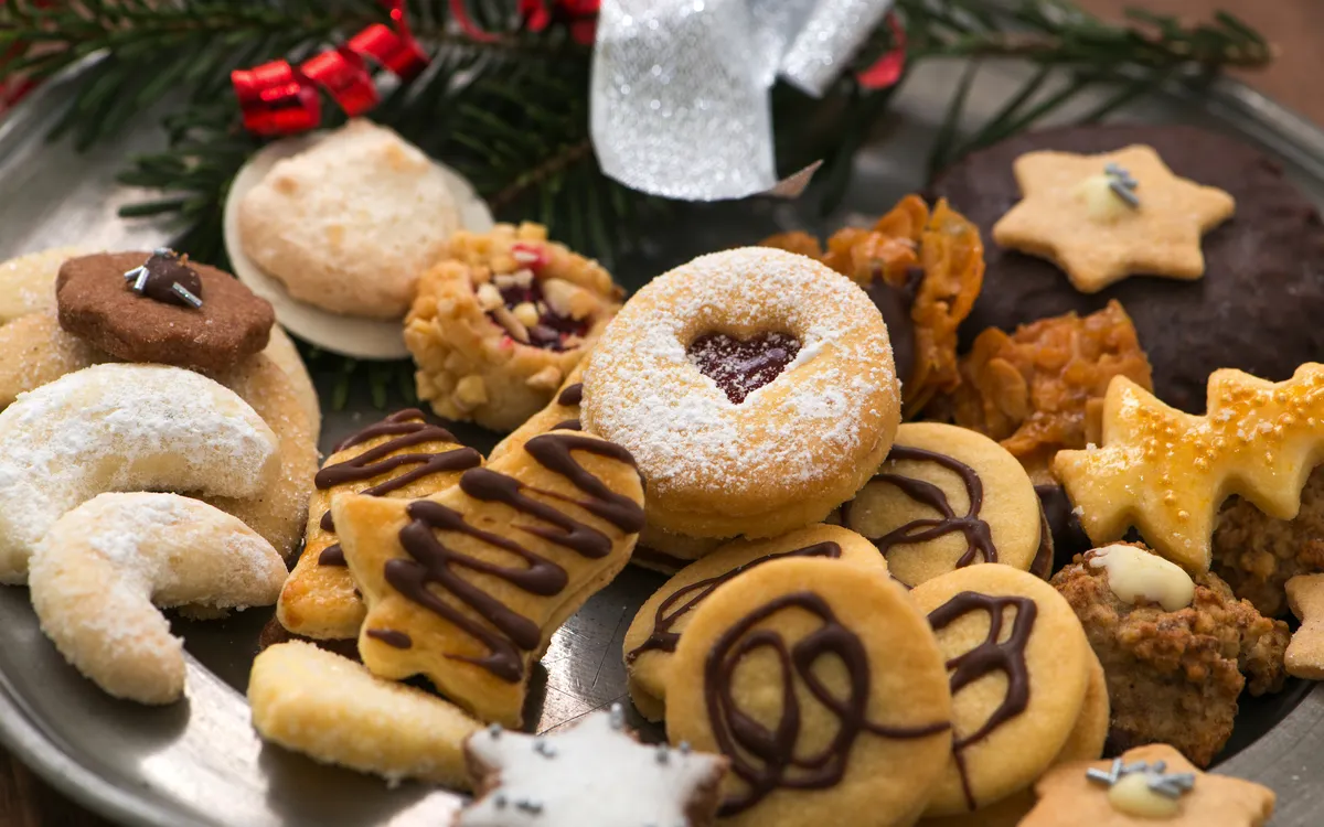 Verschiedene Weihnachtsplätzchen auf einem Teller mit Tannenzweig-Dekoration.