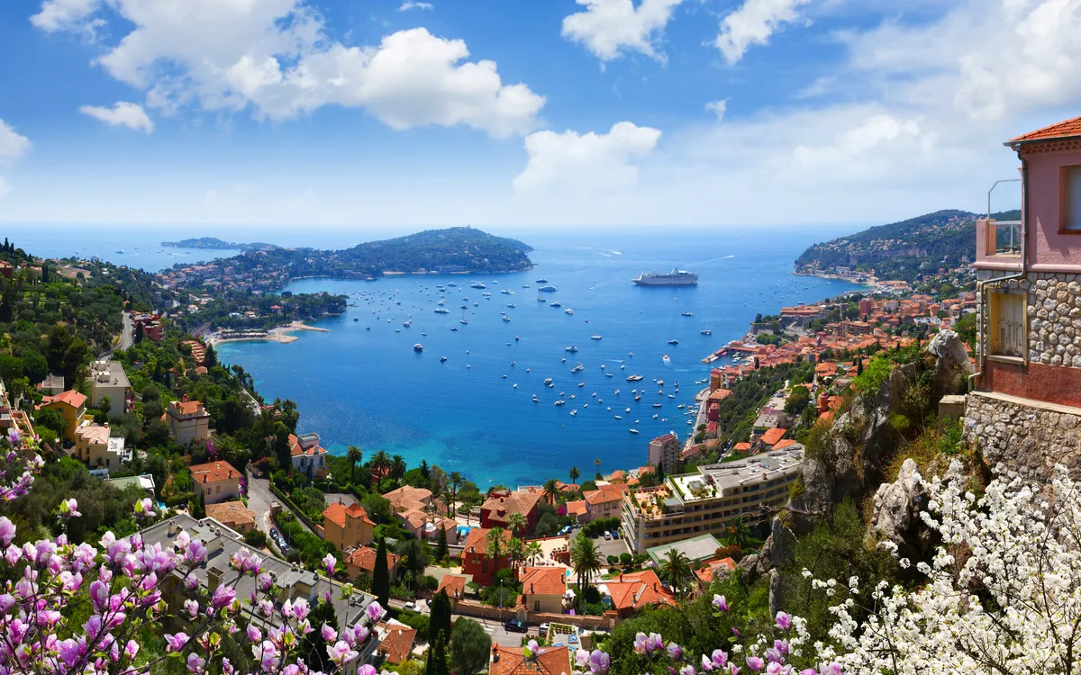 Küstenstadt mit Häusern, Blumen und Schiff in einer Bucht an einem sonnigen Tag