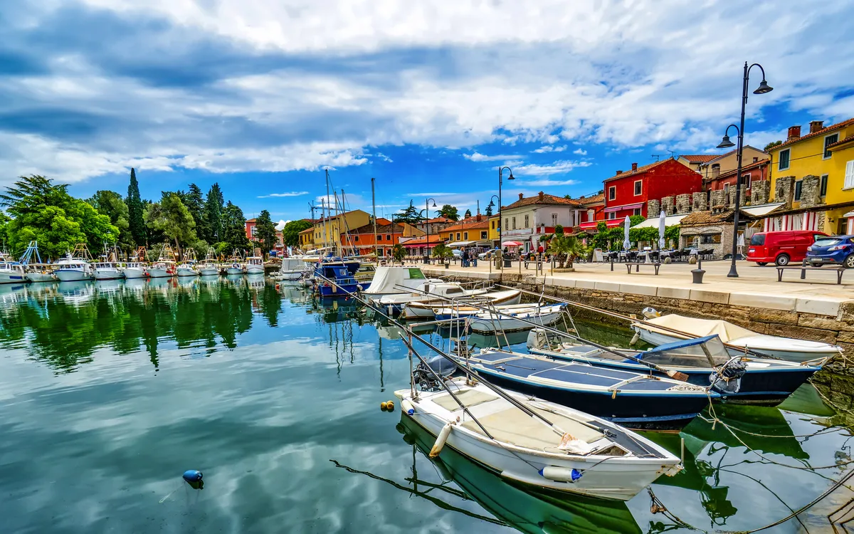Boote an einem ruhigen Hafen mit bunten Gebäuden und Wolken am Himmel.