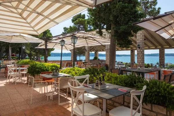 © Aminess Hotels / Pressebild Außenterrasse mit Tischen und Stühlen am Meer unter Sonnenschirmen.