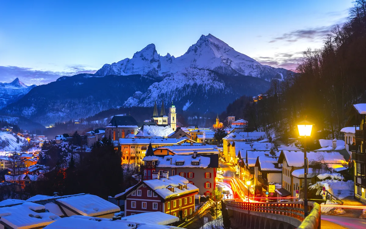 Verschneite Bergstadt bei Dämmerung mit beleuchteten Häusern und Kirche.