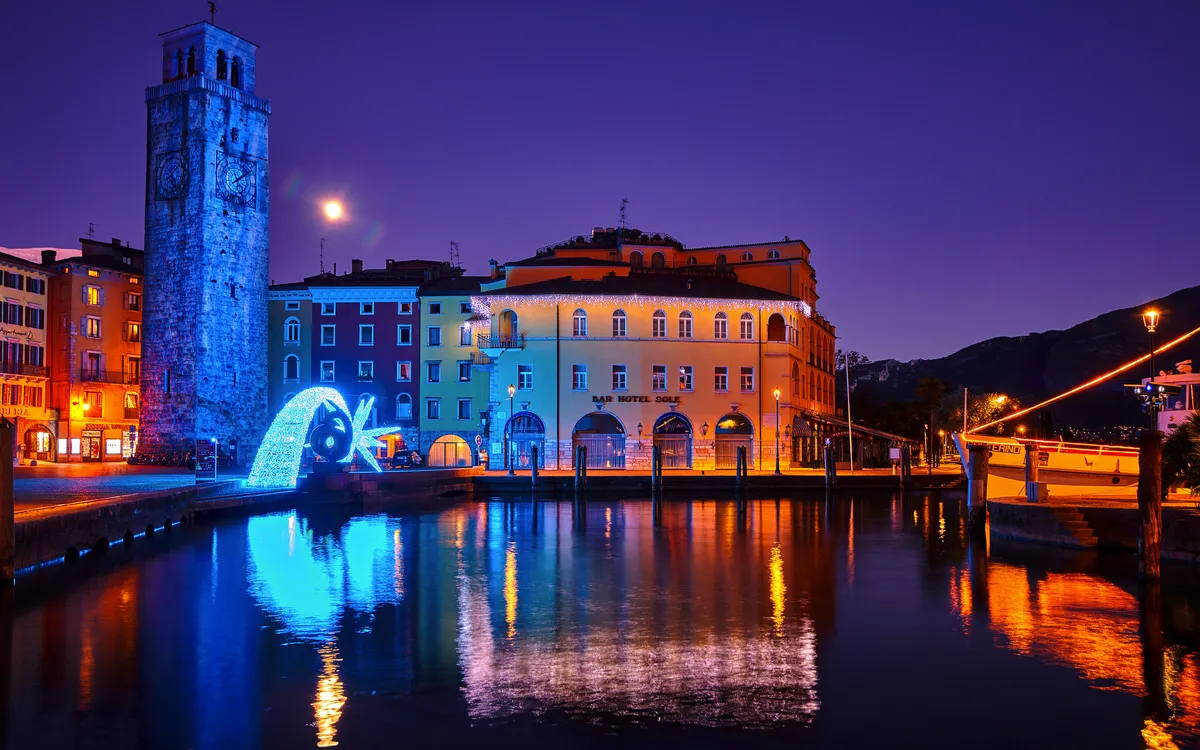 Beleuchtete Stadtansicht am Abend mit einem beleuchteten Turm und Wasserreflexionen.