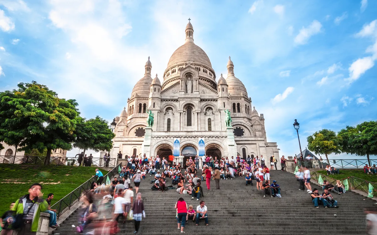 Sacré-Cœur Basilika in Paris mit vielen Besuchern auf den Treppen davor.