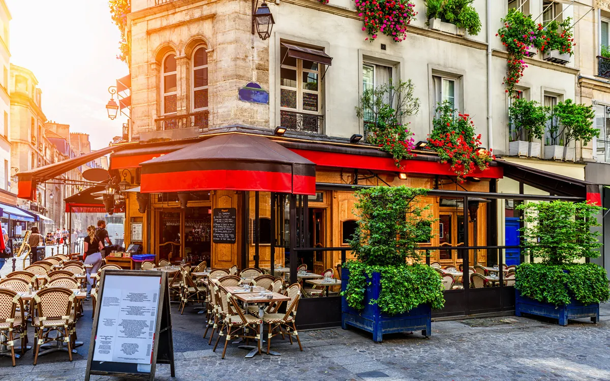 Straßencafé in einem historischen Gebäude mit roten Markisen und blühenden Pflanzen.