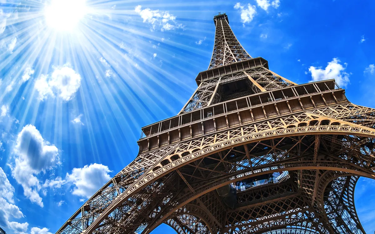 Blick von unten auf den Eiffelturm in Paris bei klarem Himmel und Sonnenschein.
