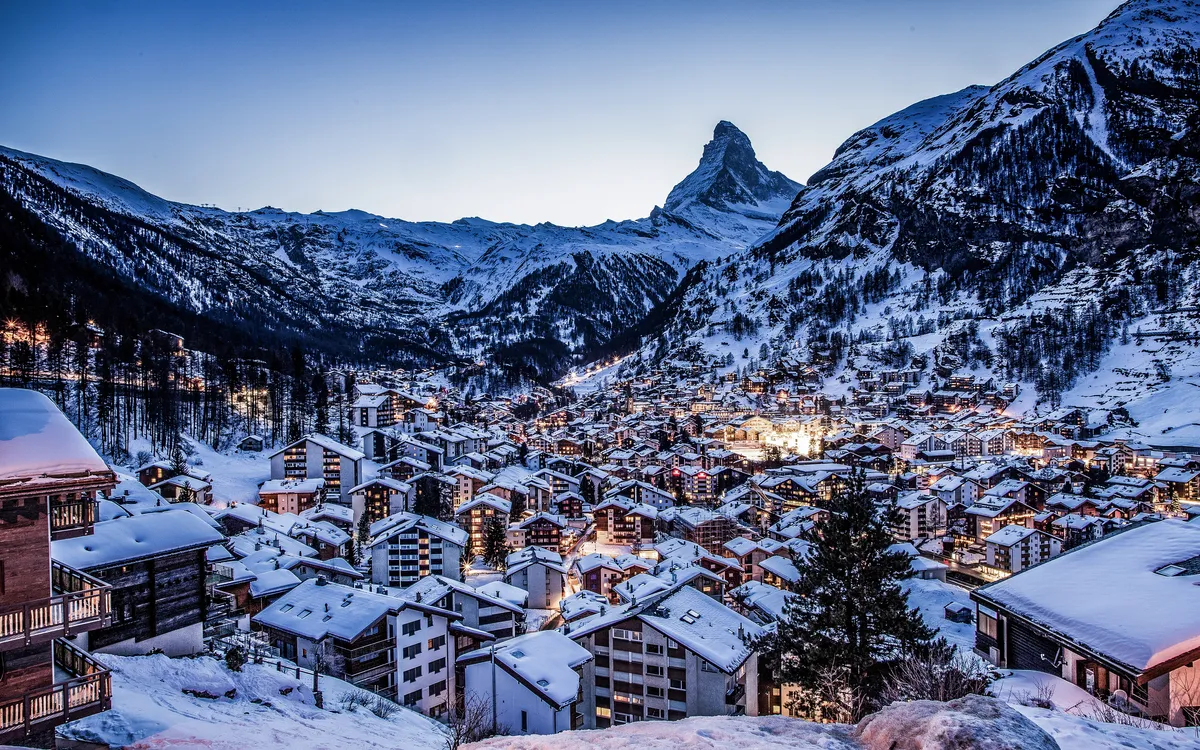 Verschneite Berglandschaft mit Dorf im Abendlicht, Matterhorn im Hintergrund.