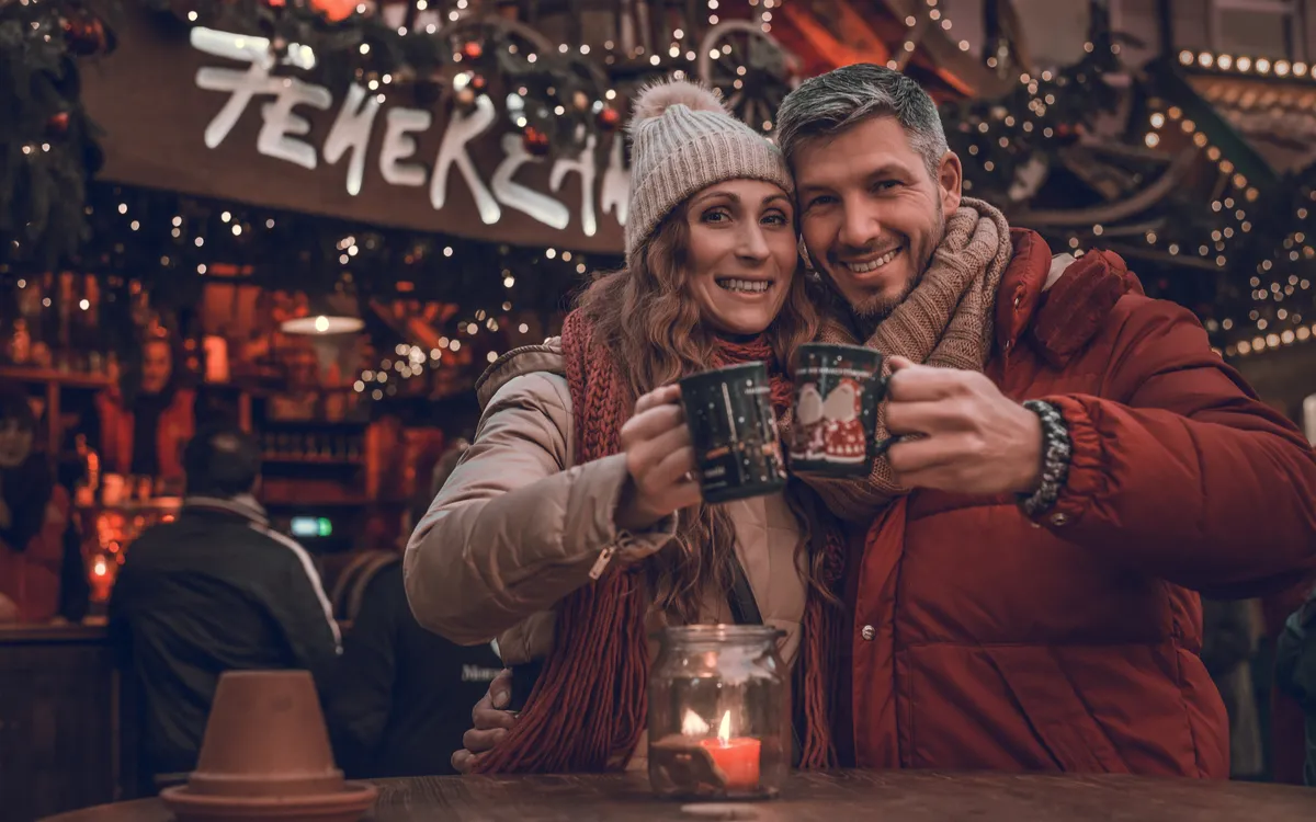Paar auf Weihnachtsmarkt mit Glühwein in festlicher Atmosphäre.