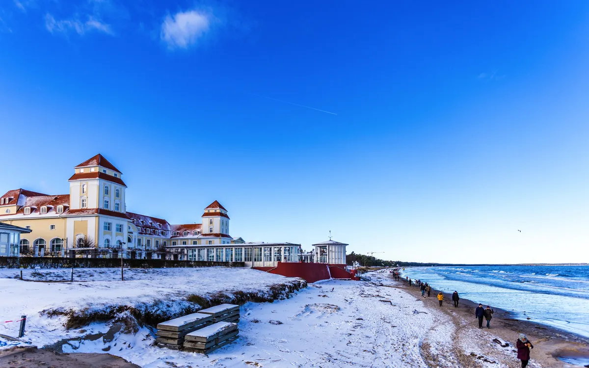 Winterlicher Strand in Binz auf Rügen mit Promenade und verschneiten Gebäuden.