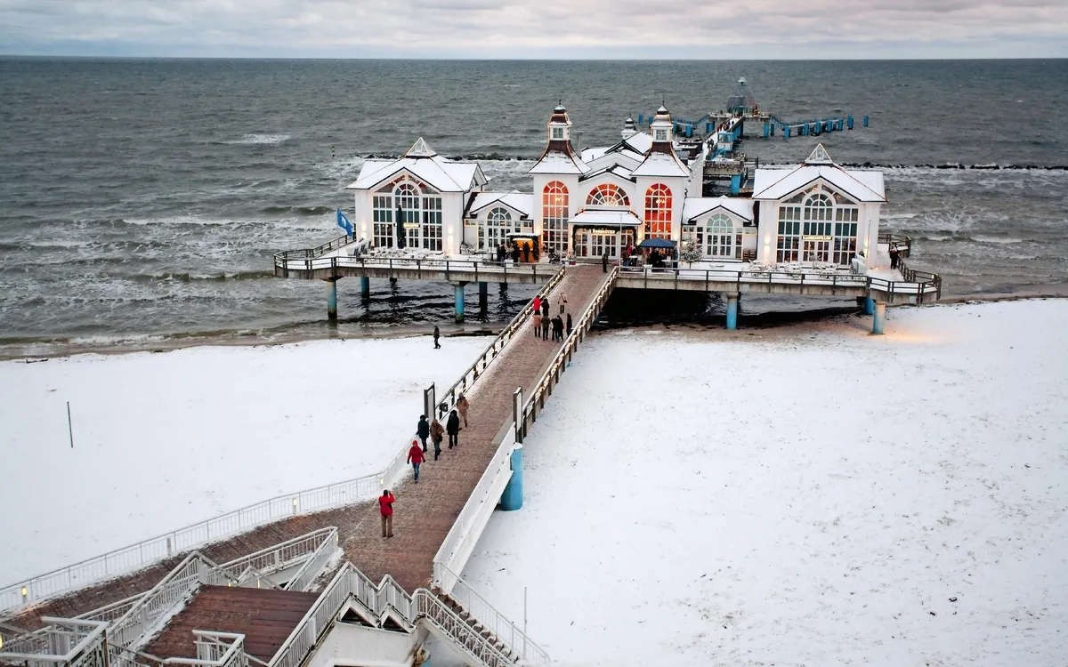 Seebrücke mit verschneitem Strand und Meer im Hintergrund.