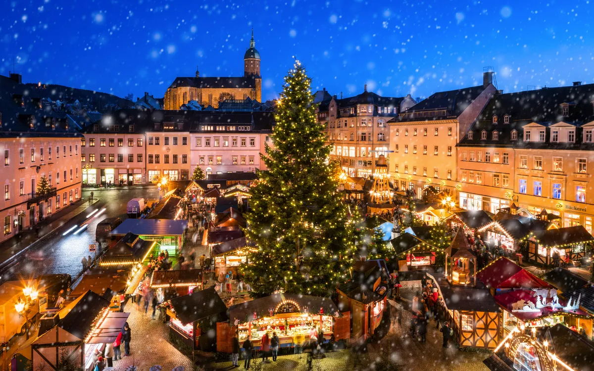 Festlich beleuchteter Weihnachtsmarkt bei Schneefall in historischem Stadtzentrum.