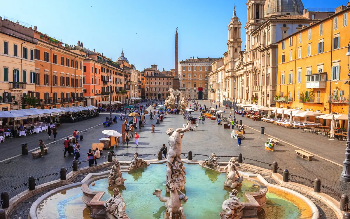 Piazza mit Brunnen und historischen Gebäuden bei sonnigem Wetter.