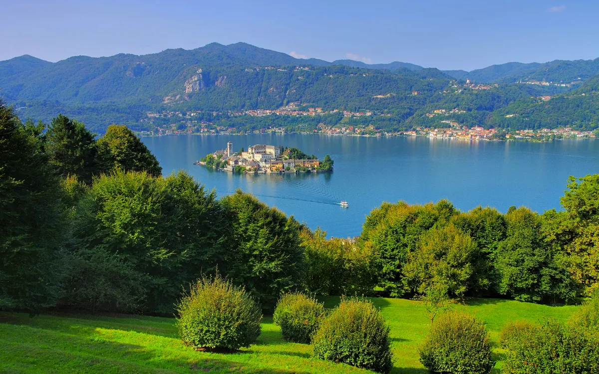 Grüne Wiese mit Blick auf einen See und eine Insel, umgeben von Bergen.