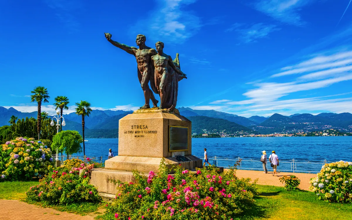 Statue vor einem See mit Bergen im Hintergrund bei klarem Himmel.