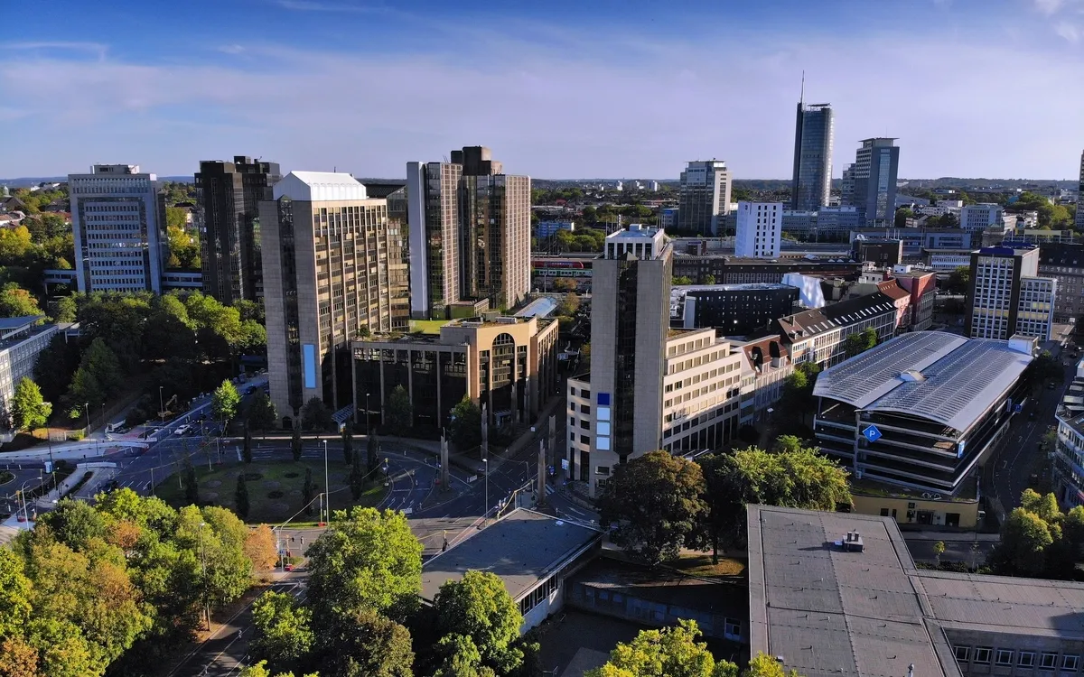 Luftaufnahme einer Stadt mit modernen Hochhäusern und grünen Bäumen.