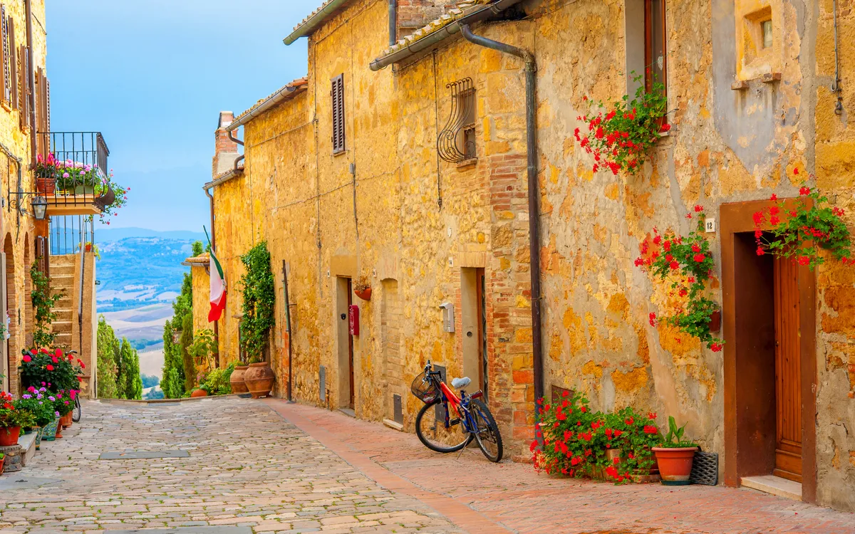 Malerische Gasse mit alten Gebäuden und Blumen, Fahrrad an einer Wand gelehnt.