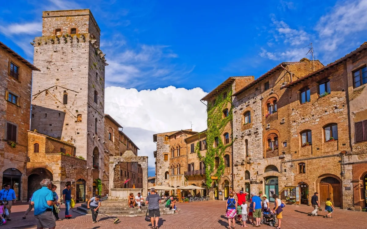 Historischer Platz mit alten Gebäuden, Touristen und blauem Himmel.