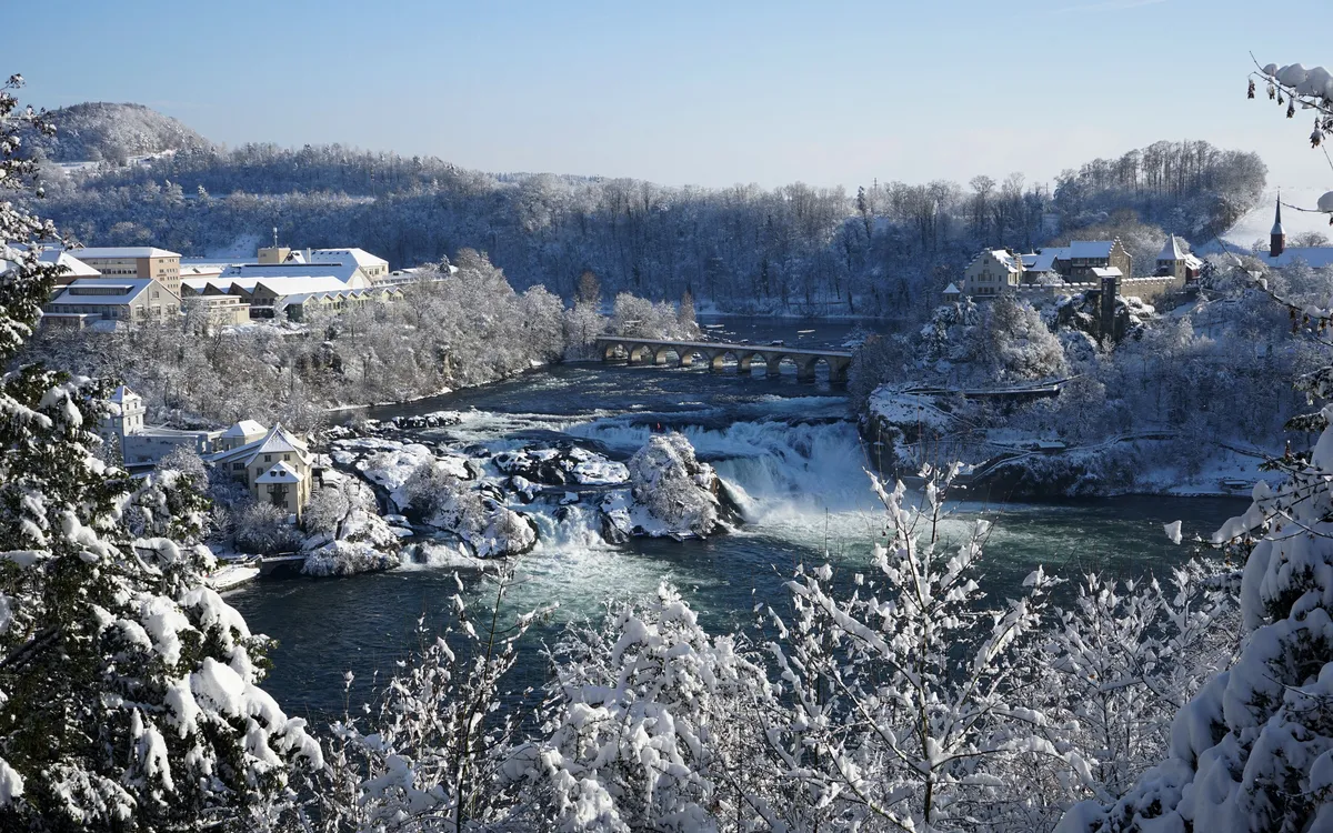Verschneite Landschaft mit Wasserfall und Brücke im Winter.