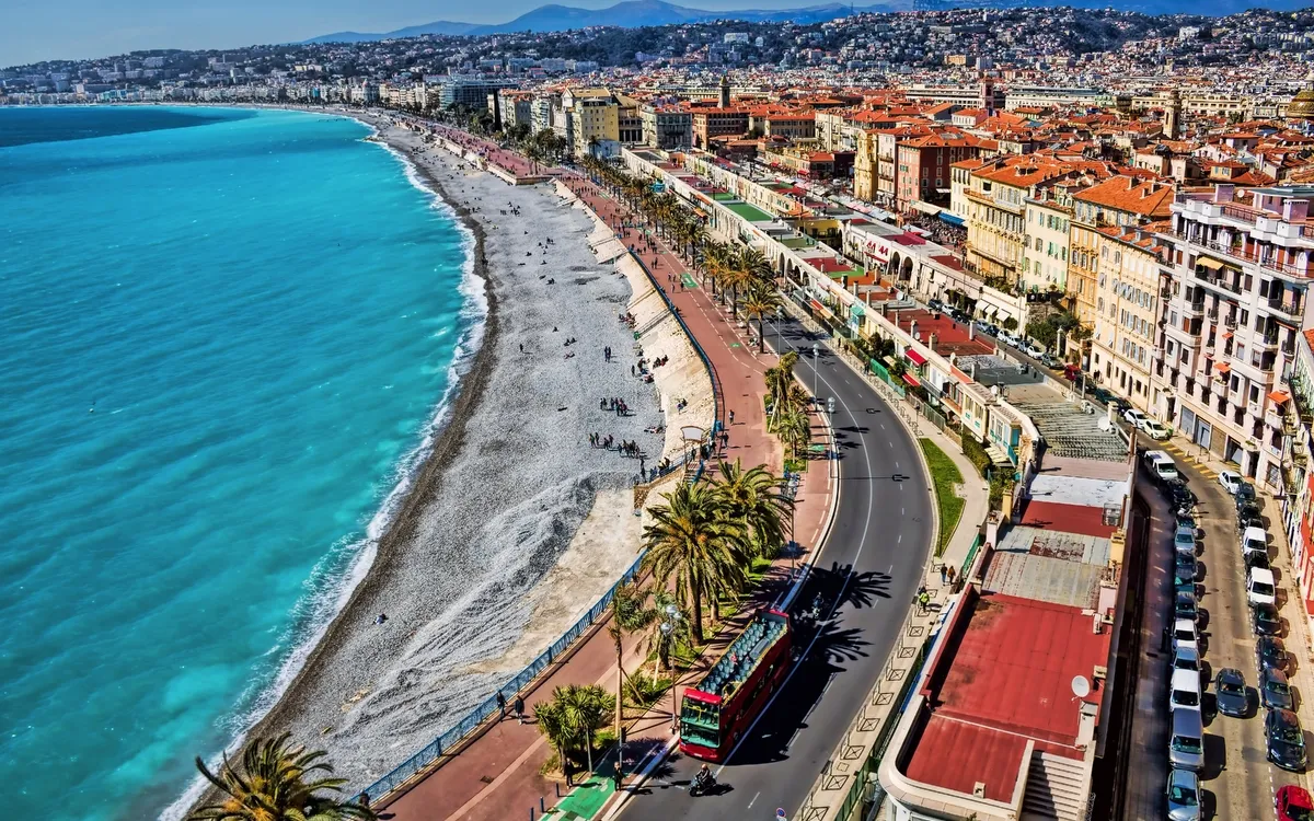 Strandpromenade mit blauem Wasser und Stadt im Hintergrund.