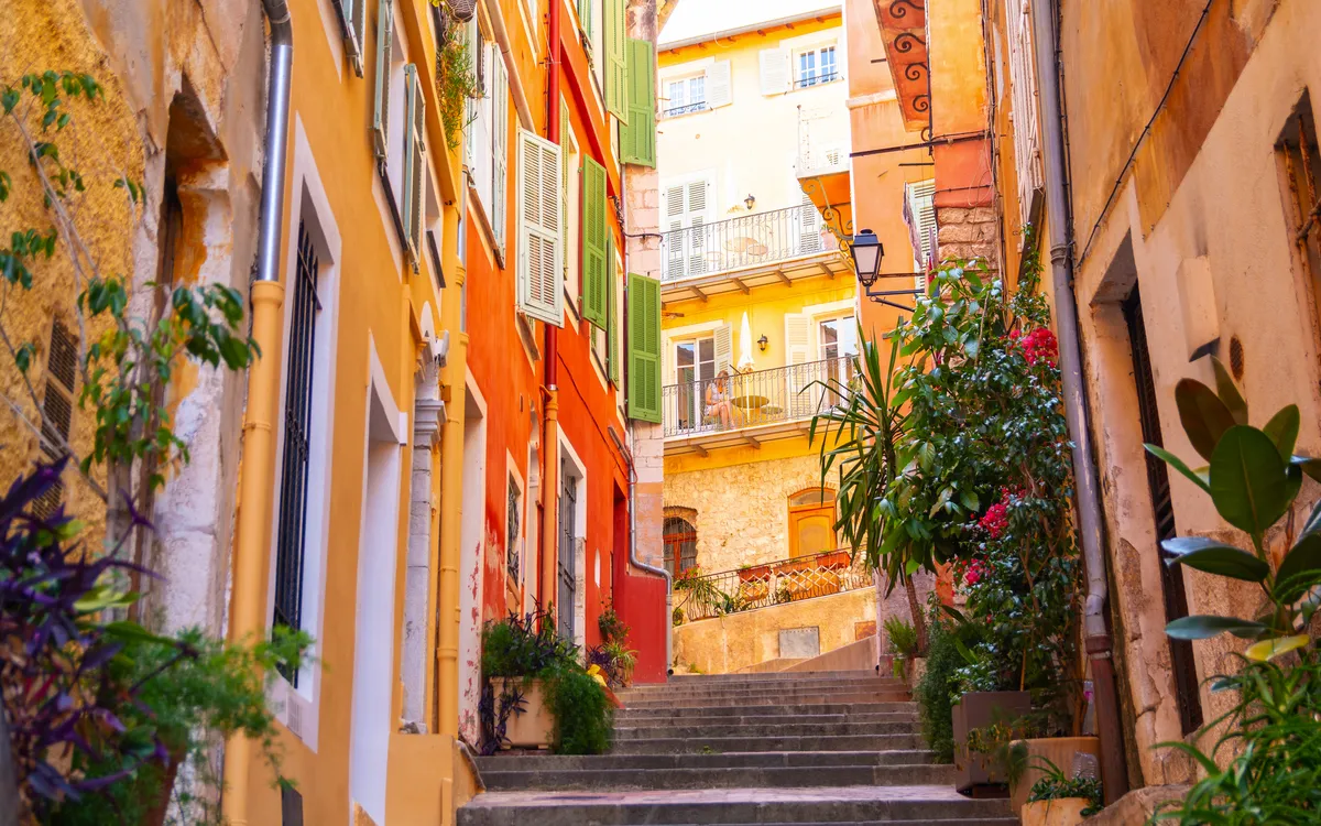 Bunte Häuser an enger, steiler Gasse mit Treppen und Pflanzen.