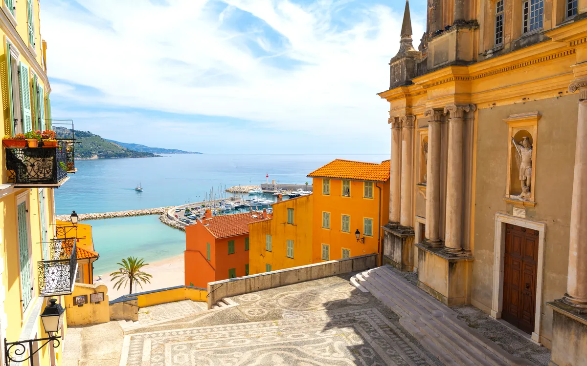 Blick auf mediterrane Küstenstadt mit bunten Gebäuden und Meer im Hintergrund.