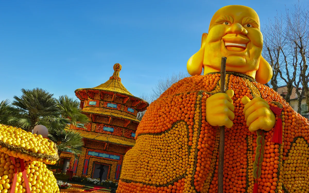 Statue eines lächelnden Buddhas aus Zitrusfrüchten, Pagode im Hintergrund.