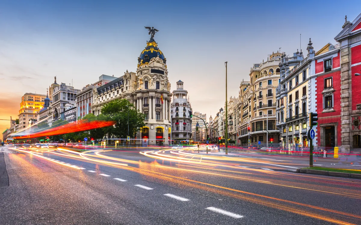 Straßenszene in Madrid bei Sonnenuntergang mit historischen Gebäuden und Lichtspuren.