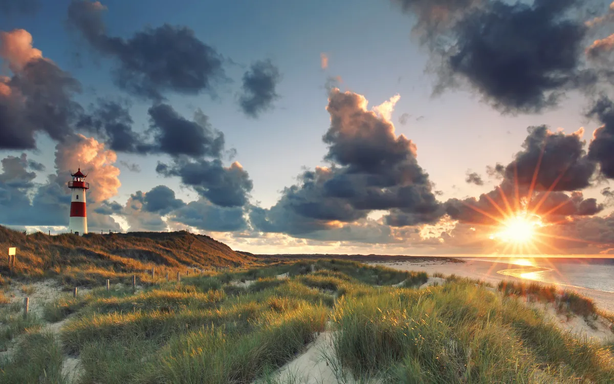 Leuchtturm am Strand bei Sonnenuntergang mit Wolkenhimmel